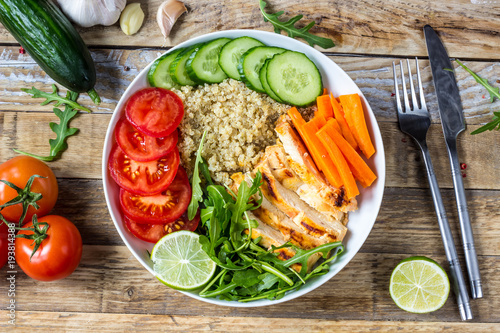 Healthy salad bowl with quinoa, tomatoes, chicken, cucumber, lime and arugula