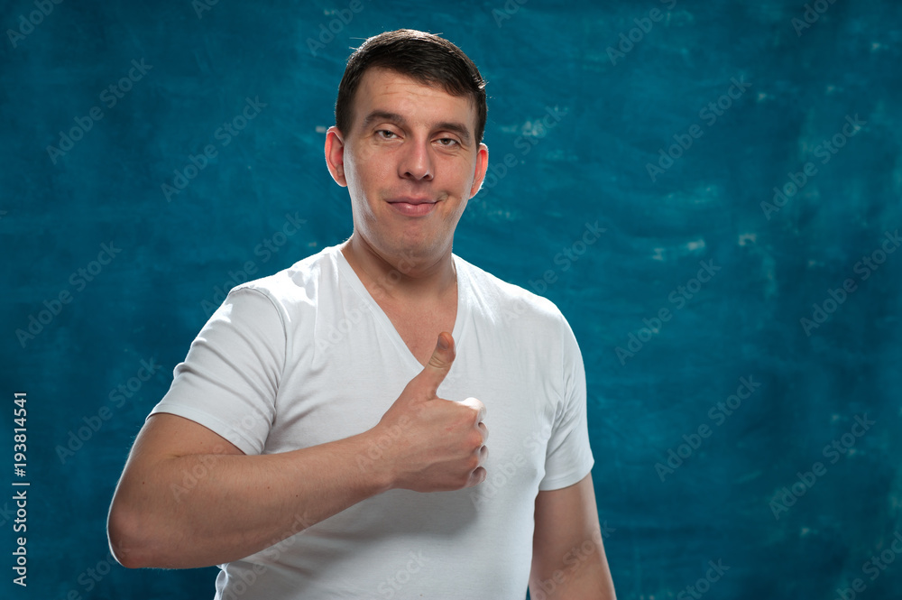 Portrait of positive man in white shirt showing thumbs up gesture on blue background. Place for text Portrait of positive man in white shirt showing thumbs up gesture on blue background. Place for text