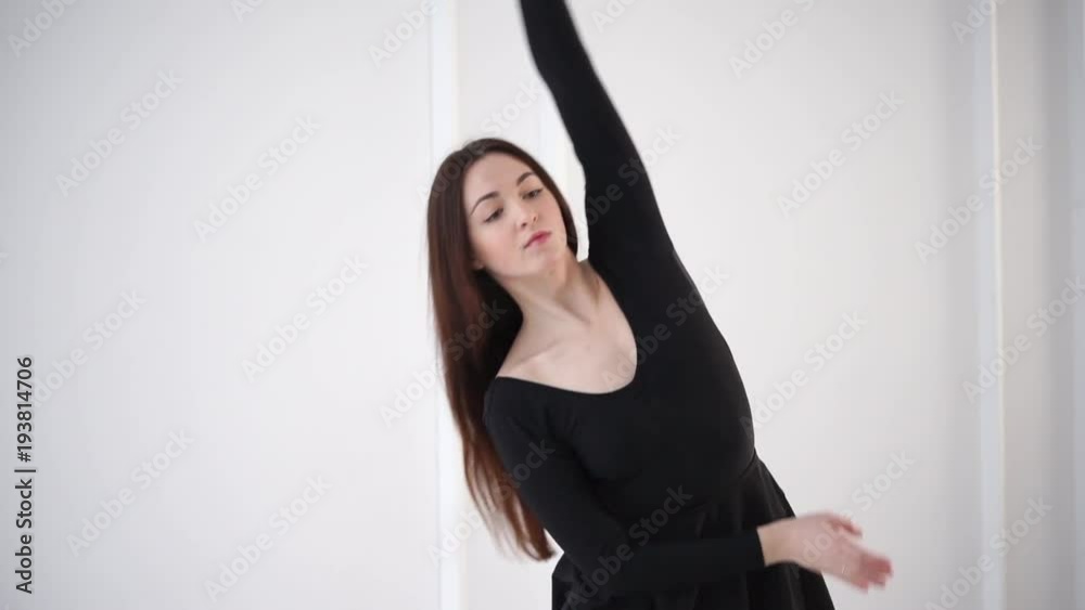 Engaging brunette dancer is stretching in completely white studio wearing black. She is tilting to sides. Engaging brunette dancer is stretching in completely white studio wearing black. She is tilting to sides.