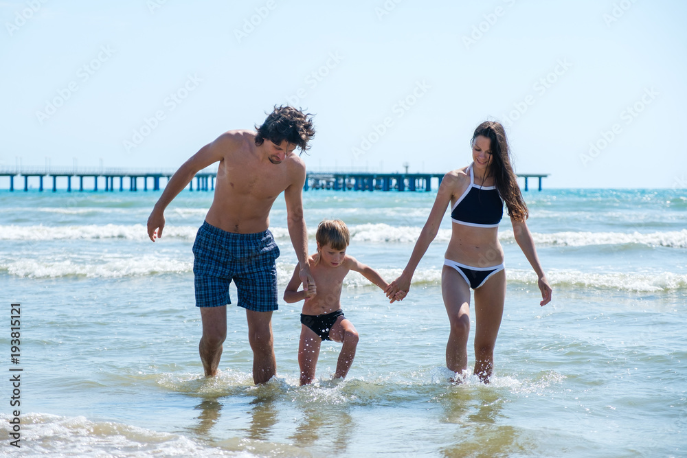 Mom, dad and son splashing in the sea on warm sunny day. Holding hands together