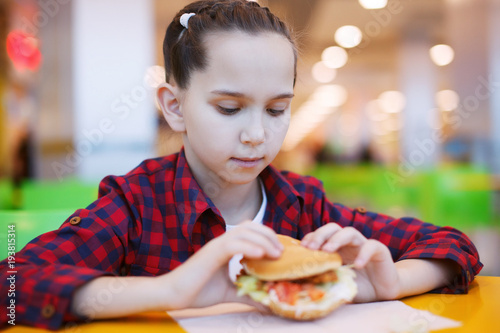 Cute smiling little girl eats a hamburger