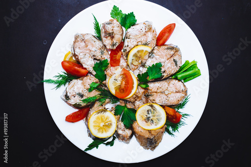 Baked salmon fish fillet with tomatoes, spices., lemon on a white plate on a black background. Diet menu.