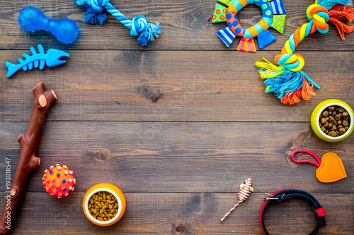 Pet accessories. Toys near bowls with animal feed, collar on dark wooden background top view copy space