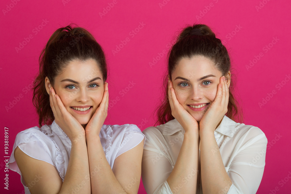 two beautiful young sisters twins in a good mood in white blouses on a pink background two beautiful young sisters twins in a good mood in white blouses on a pink background