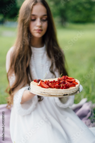 Tender sensitive girl with blue eyes on a picnic with sweet creamy cheesecake with peonies