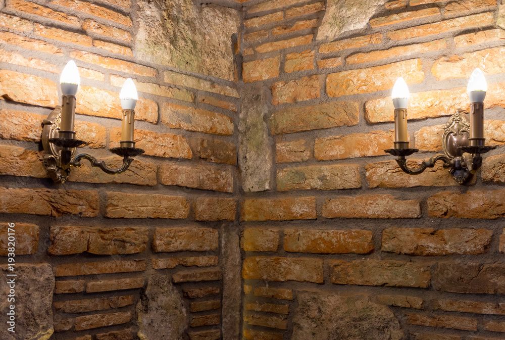Two candlesticks with lamps in corner of brick wall in ancient building