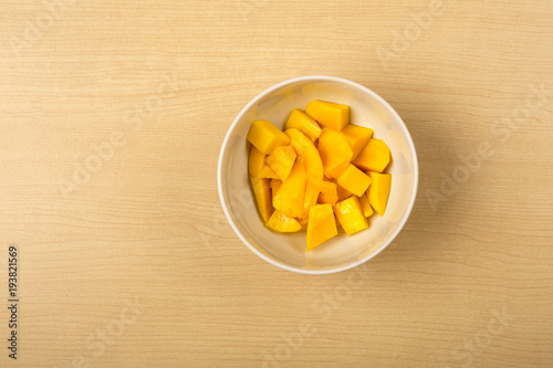 Fresh mango chopped in a white bowl on wood background, clean food, view from above