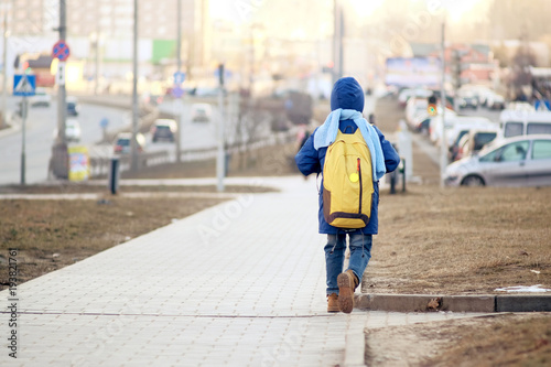 kid (boy) in blue jacket and blue scarf with yellow bagpack going to school in spring, copy space