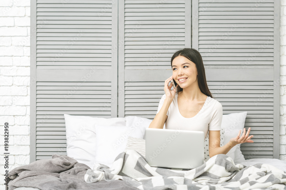 Happy casual beautiful woman working on a laptop sitting on the bed in the house. Working at home. Freelance concept. Happy casual beautiful woman working on a laptop sitting on the bed in the house. Working at home. Freelance concept.