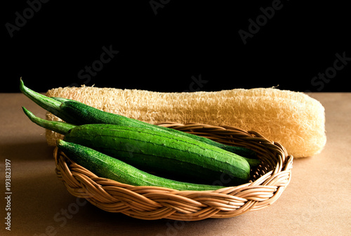 Luffa cylindrica (L.) M.J.Roem and Trichosanthes anguia Linn. Green fresh in basket weave with dry sponge gourd. Black background and shadow. photo