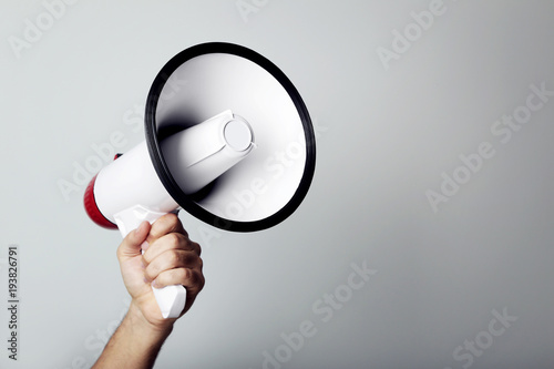 Female hand holding megaphone on grey background photo
