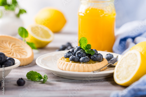 Homemade shortbread tartlet with lemon curd and fresh blueberries on white wooden background. Holiday food concept.