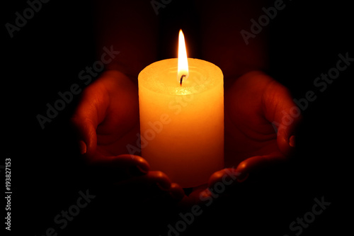 Female hands holding burning candle on black background