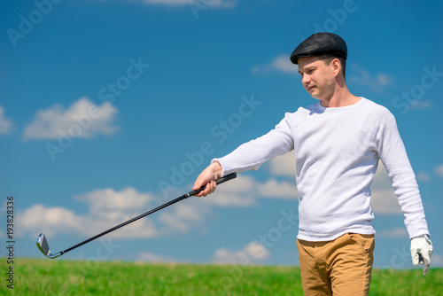 Young golfer in a cap and golf club on a green playing field