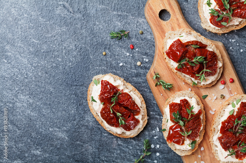 Bread slices with cream cheese and sun dried tomatoes on wooden table top view. Delicious snack and appetizer. photo