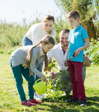 Adult parents with two kids placing a new tree
