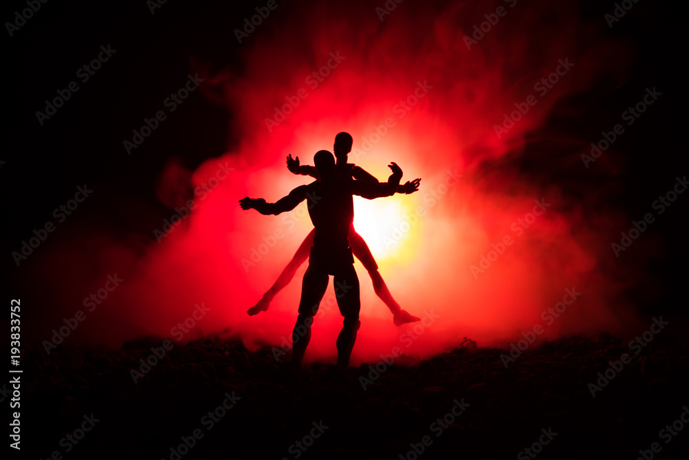 Love Valentine`s Day concept.Sillhouette of sweet young couple in love standing in the field and hugging on dark toned foggy background. Decoration with doll figures on table shot.