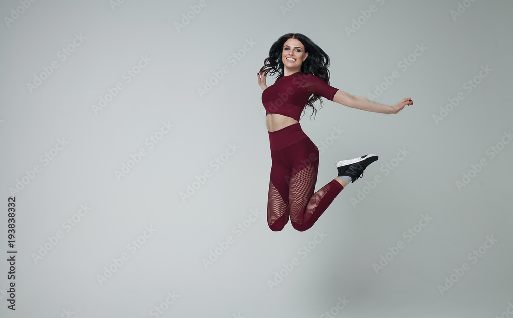 Portrait of fit and sporty young woman jumping on grey background.