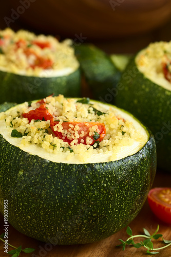 Baked round zucchini stuffed with couscous, cherry tomato and parsley, photographed with natural light (Selective Focus, Focus on the cherry tomato on the first stuffed zucchini)