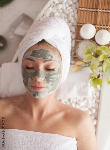 Young healthy woman in spa making treatments and face clay mask.