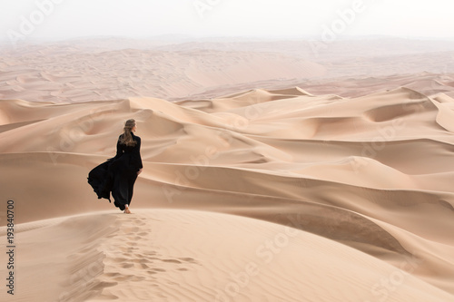Fotografia Young beautiful Caucasian woman posing in a traditional Emirati dress - abaya in Empty Quarter desert landscape