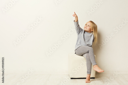 Fototapeta Naklejka Na Ścianę i Meble -  Happy little girl pointing aside at white studio background