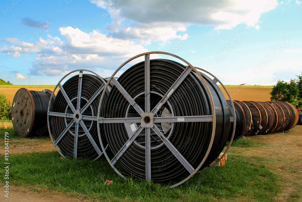 Black wire electric cable with wooden coil of electric cable under the sky Black wire electric cable with wooden coil of electric cable under the sky