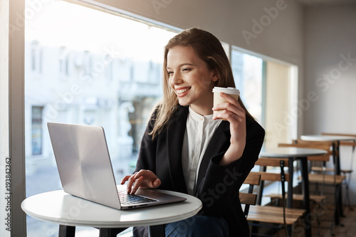 Free Download Best place in city with free wifi. Portrait of beautiful stylish urban businesswoman, sitting in cafe, holding cup of coffee and working with laptop, smiling joyfully Catching up with online life - GFXLoad