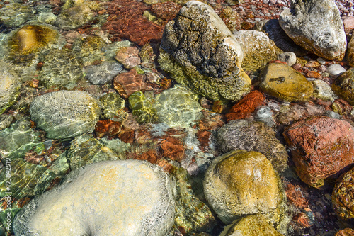 Transparent sea water seethes at the shore. Large coastal colored stones in the water. Beautiful abstract background.
