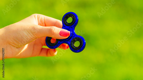 Girl playing blue metal spinner in hands on the street, female hands holding popular fidget spinner toy on green background, anxiety relief toy, anti stress and relaxation fidgets