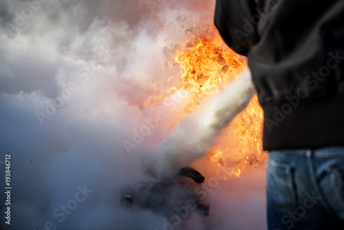 man from behind is fighting a fire with foam from a fire extinguisher, copy space in the smoke