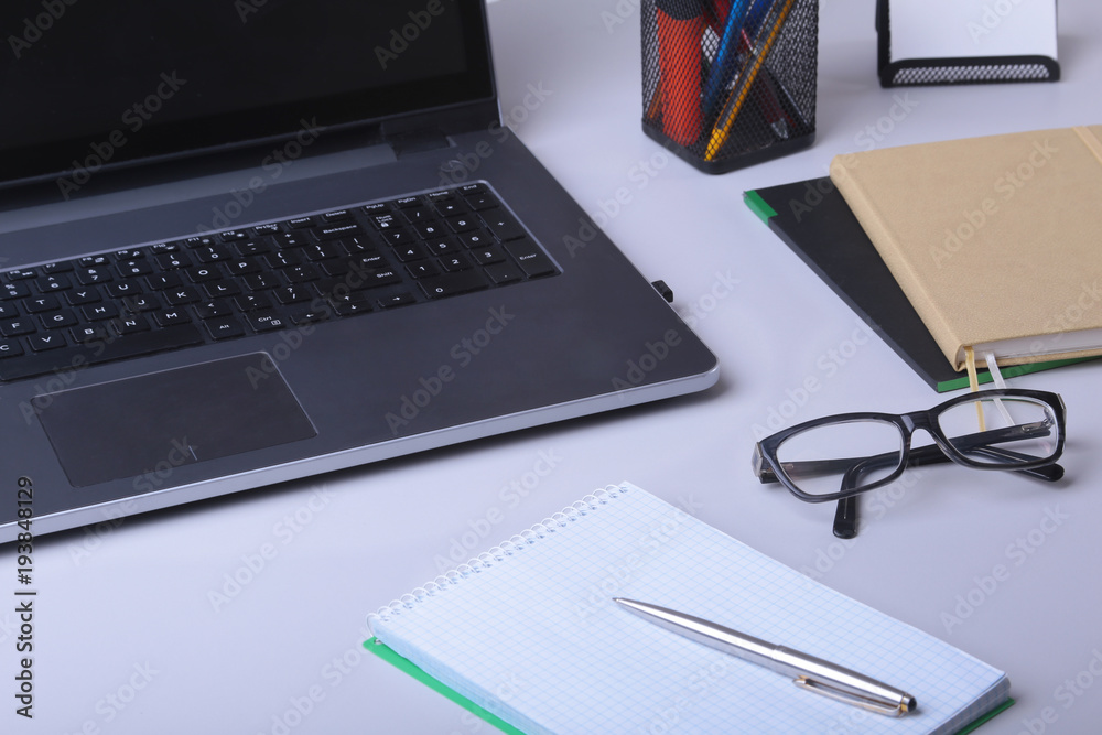 Close-up of comfortable working place in office with laptop, mouse, notebook, glasses, pen and other equipment laying on table on blur furniture background. Close-up of comfortable working place in office with laptop, mouse, notebook, glasses, pen and other equipment laying on table on blur furniture background.