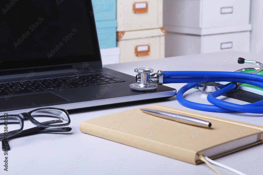 Workplace of doctor with laptop, stethoscope, RX prescription, glasses and red heart and notebook on white table. Copy space. Workplace of doctor with laptop, stethoscope, RX prescription, glasses and red heart and notebook on white table. Copy space.