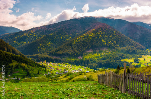 village in valley on a cloudy springtime day. fence on hillside above beautiful rural area