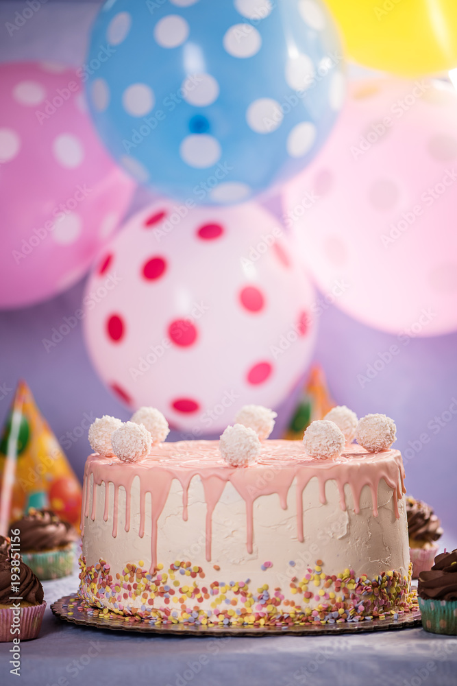 detail of a pink white birthday cake with coconut balls colorful balloon background