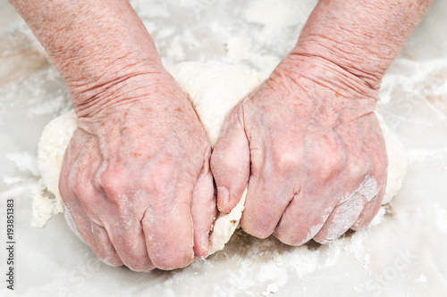 Female senile hands knead the dough on a table, close-up