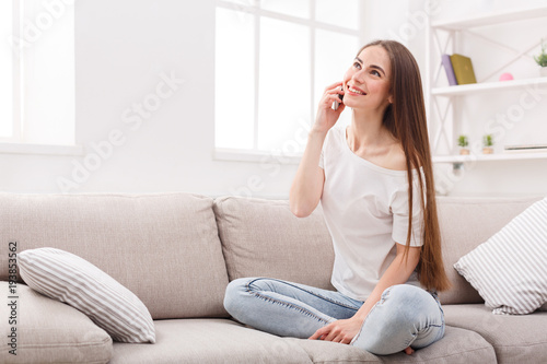 Young woman sitting on sofa and talking on cell phone