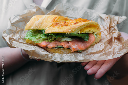 Sandwich with salmon on kraft paper in the hands of a woman