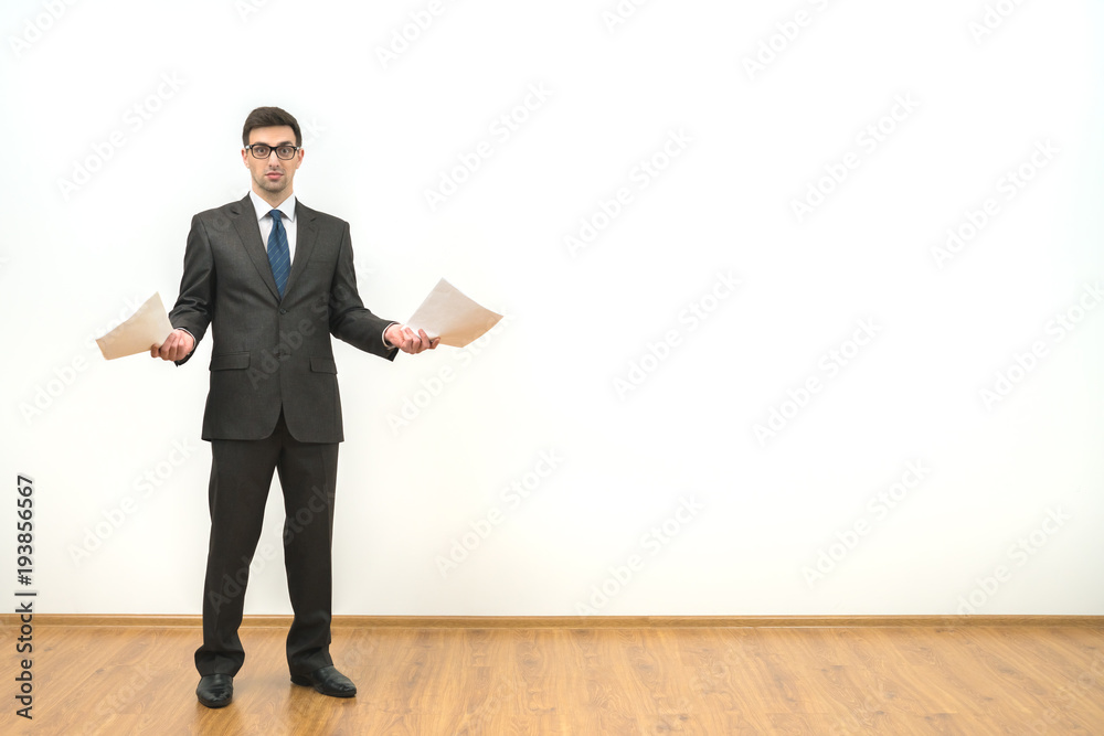 The businessman holds papers on the white wall background The businessman holds papers on the white wall background