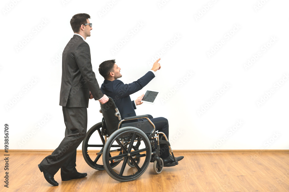 The man and a disabled with a tablet gesturing on the white wall background The man and a disabled with a tablet gesturing on the white wall background