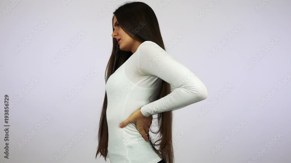 A young beautiful woman rubs her aching back - closeup - white background A young beautiful woman rubs her aching back - closeup - white background