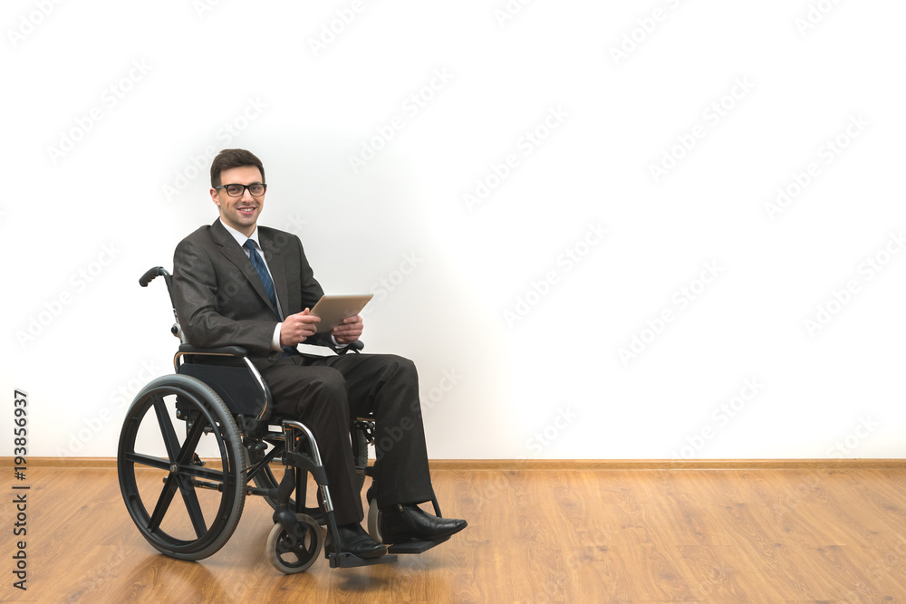 The smile disabled in the wheelchair holding a tablet on a white wall background The smile disabled in the wheelchair holding a tablet on a white wall background