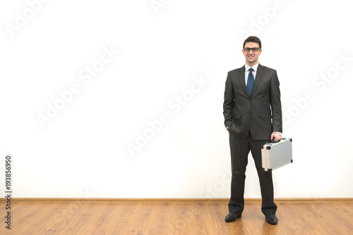 The businessman with a case standing on the white wall background