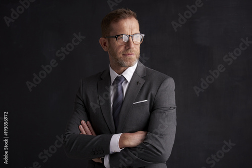 Executive senior businessman portrait. Middle aged financial director business man wearing suit and looking at camera while standing at dark background. 