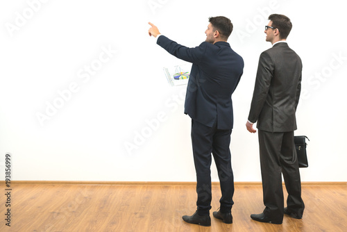 The two businessmen with papers gesture on the white wall background