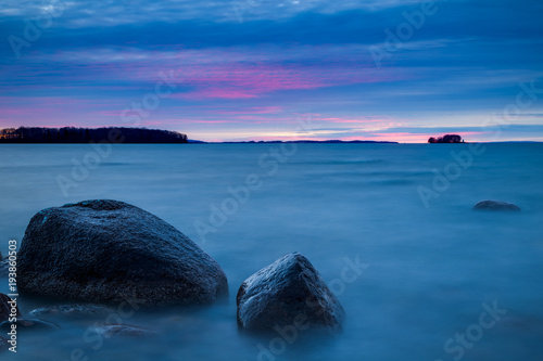 Long exposure of a sunset at the coast with a rock in the foreground