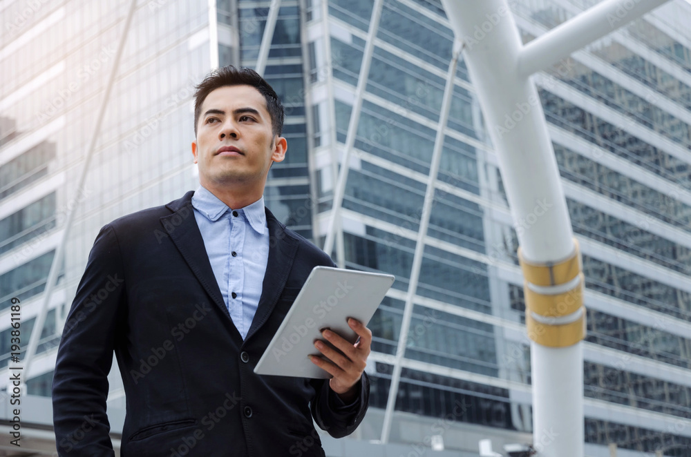 young handsome asian business man wearing modern black suit reading information about finance news with mobile tablet in building city background, network technology, internet, successful concept young handsome asian business man wearing modern black suit reading information about finance news with mobile tablet in building city background, network technology, internet, successful concept