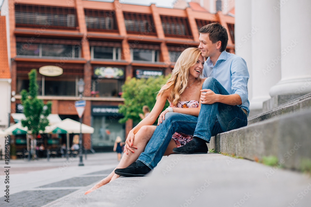 Young happy couple hugging on the street sitting on the stairs. Smiling man and woman having fun in the city.