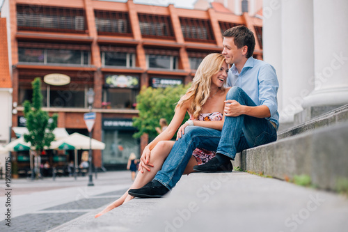 Young happy couple hugging on the street sitting on the stairs. Smiling man and woman having fun in the city.