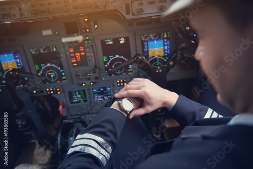 Close up male pilot looking at watch while flying plane in cockpit. Job and clock concept